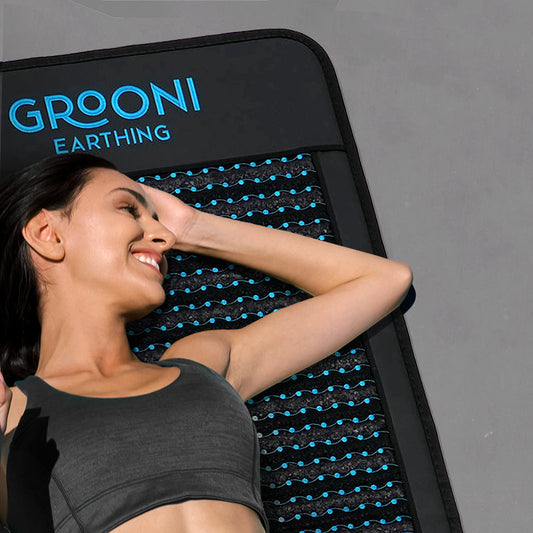 Woman relaxing on a Grooni Earthing mat with blue wavy lines, smiling and lying on her back in athletic wear.