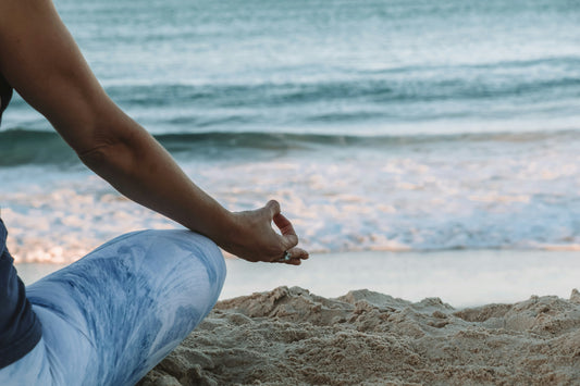 Image shows a peaceful wellness scene with a person relaxing , surrounded by calming elements like the beach and sea, illustrating a holistic mind-body routine.