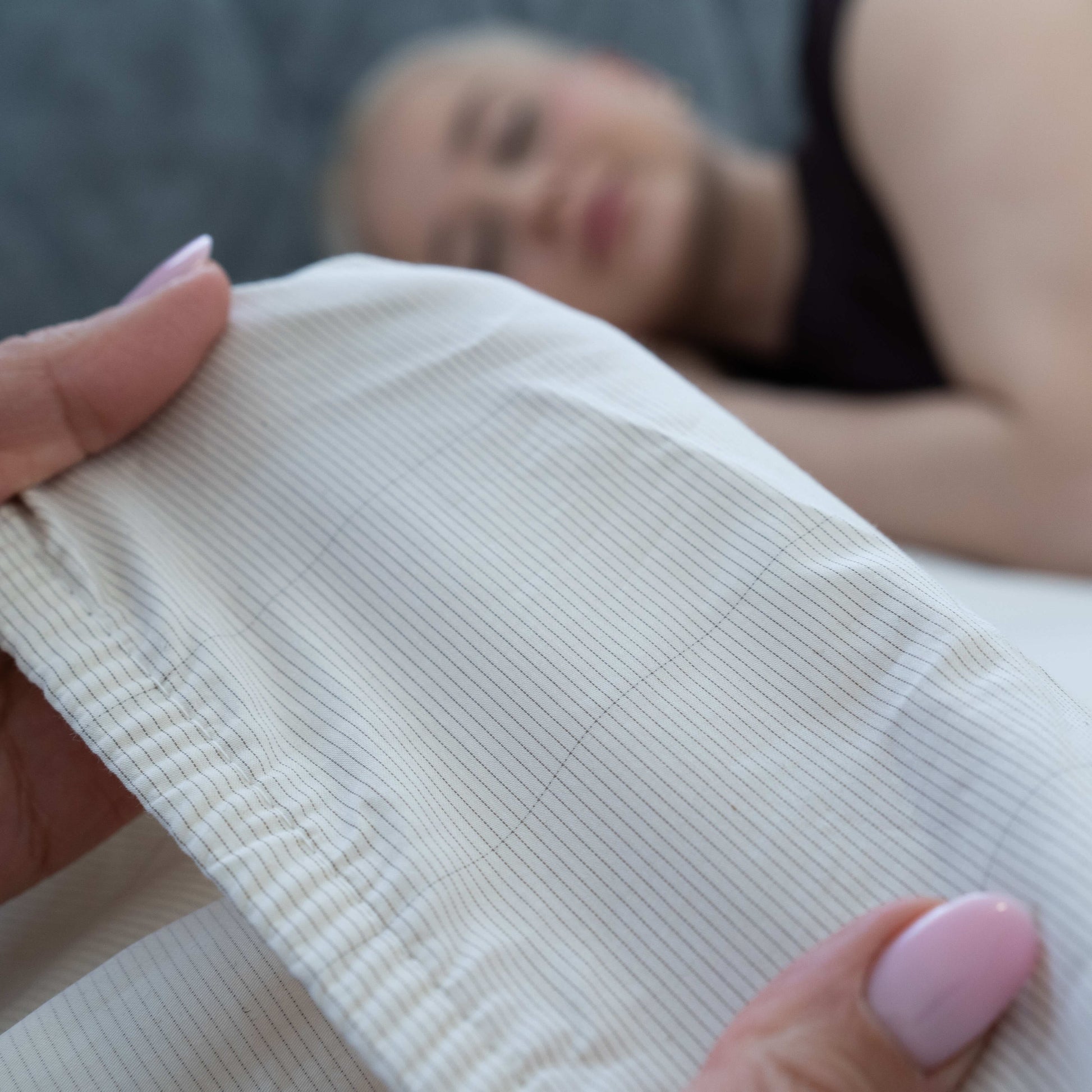 Detailed view of the fabric’s conductive silver thread woven into the Earthing Sheet with a woman sleeping in the background over the sheets