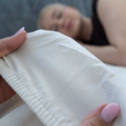 Detailed view of the fabric’s conductive silver thread woven into the Earthing Sheet with a woman sleeping in the background over the sheets