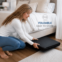 A woman in a white long-sleeve top and blue leggings kneels on a wooden floor beside a bed, folding a black mattress or mattress topper. Text on the image reads 'FOLDABLE EASY TO STORE' with a small folded mattress icon.