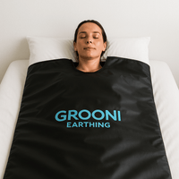 Person lying on a bed wearing a black Grooni Earthing sauna blanket.