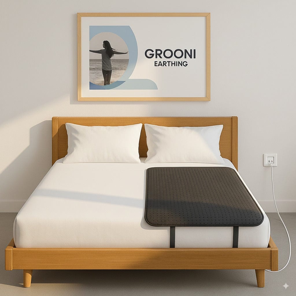 Bed with a black grounding mat on a white bedspread, framed picture above, and wall socket on a light gray wall.